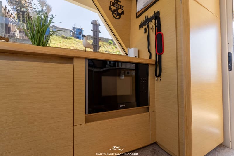 Een ingebouwde Gorenje magnetron in een houten interieur met een raam en decoraties.