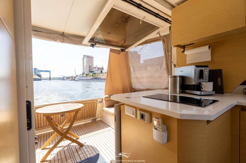Een bootinterieur met een open achterzijde, een houten klaptafel en een keukenblok met koffiezetapparaat en kookplaat.