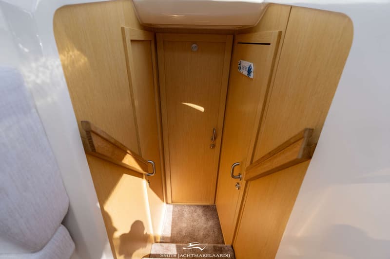 Een houten interieur met een trap naar beneden, een deur en handgrepen.