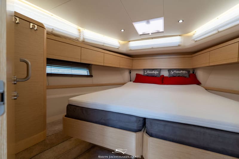 Een slaapkamer in een boot met een tweepersoonsbed, houten kasten en een raam met jaloezieën. — Greenline Greenline 39