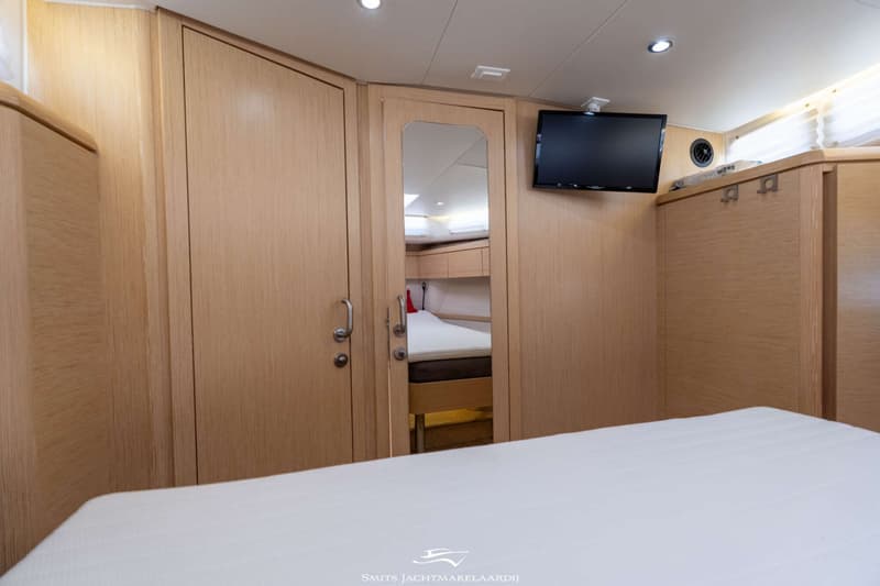 Een kajuit met een bed op de voorgrond, houten kasten en een spiegeldeur die een andere kajuit met bed reflecteert.