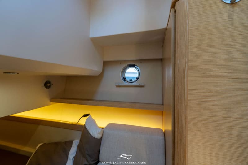 De foto toont een kajuitinterieur met een patrijspoort, een kussen en een bank, en houten panelen.