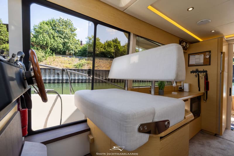 Een interieur van een boot met een stuurwiel, een witte bank en uitzicht op water en groen. — Greenline Greenline 39