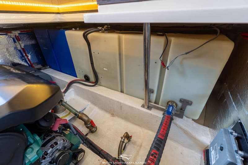 De foto toont een motorruimte met een motor, twee tanks, leidingen en bedrading.
