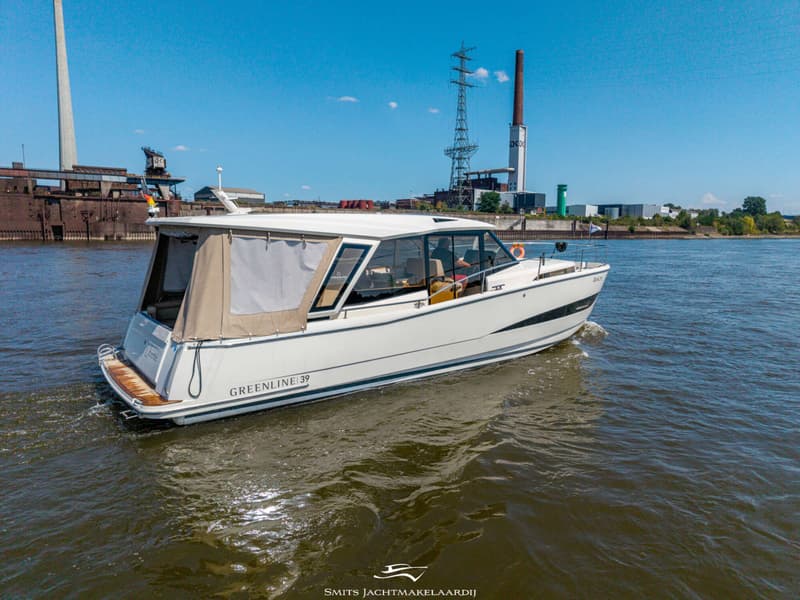 Een witte motorboot met de tekst "GREENLINE 39" vaart op water, met industriële gebouwen op de achtergrond.