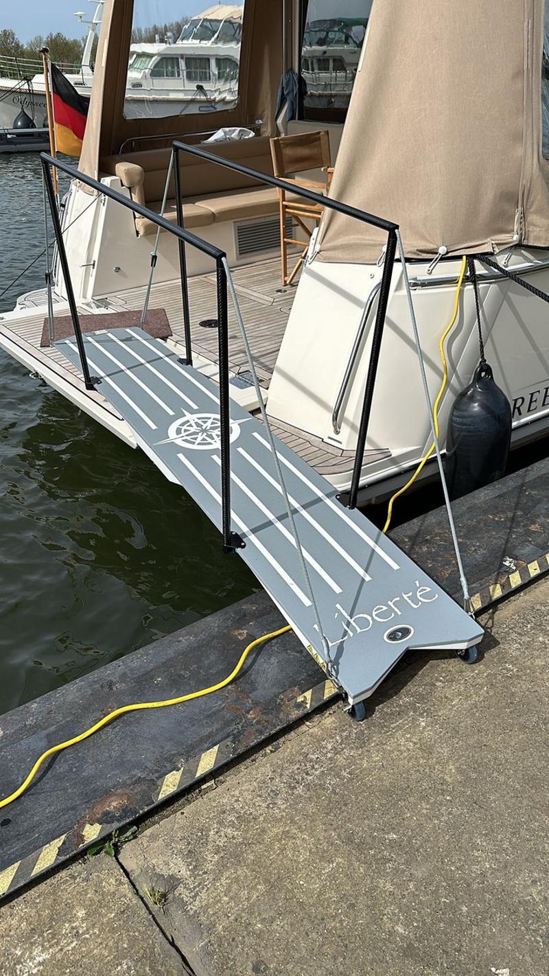 Een boot ligt afgemeerd aan een kade met een loopplank, een Duitse vlag en een stootwil. — Greenline Greenline 39
