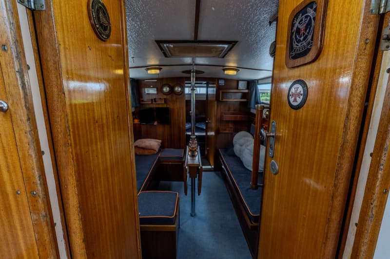 De foto toont het interieur van een boot met houten wanden en een grijze vloer, gezien door een open deur.