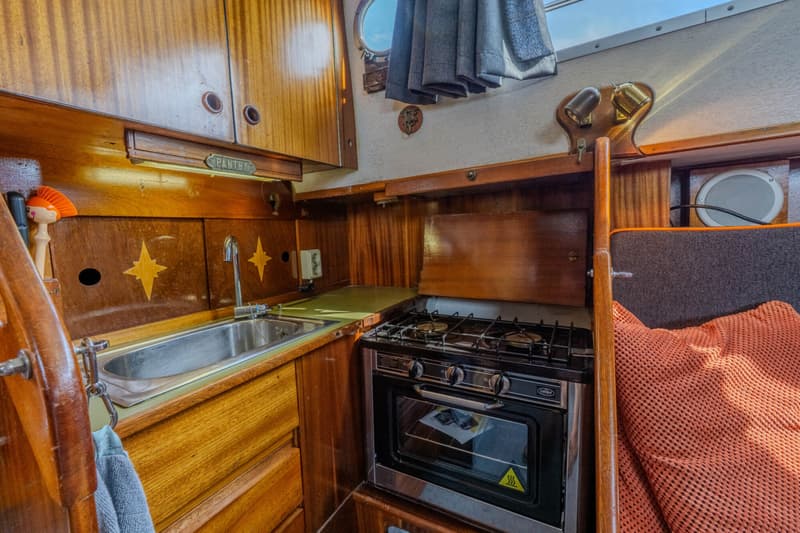 Een kombuis met een gootsteen, een fornuis met oven, houten kasten en een patrijspoort.
