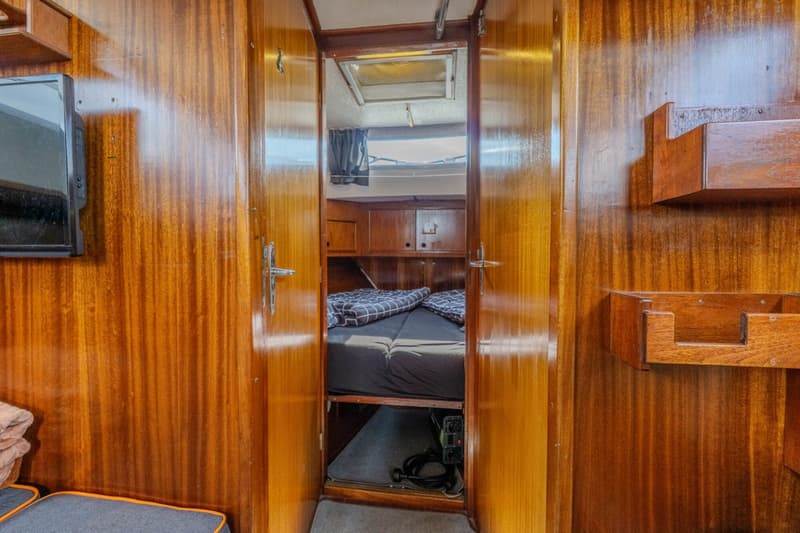 Een interieur van een boot met houten wanden, een open deur naar een slaapcabine met bed en een televisie aan de muur.