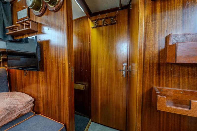 Een interieur van een boot met houten wanden, een televisie, een bank met kussens en een deur.
