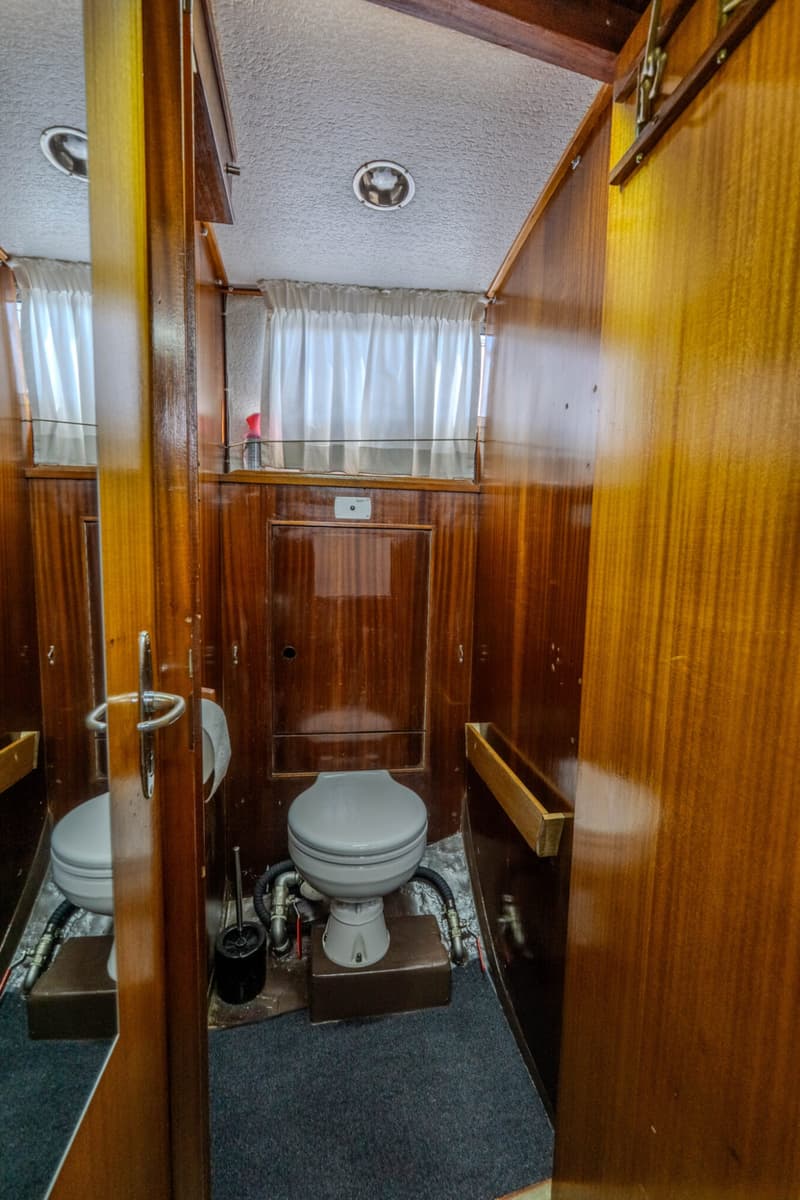 Een toiletruimte met houten wanden, een grijs toilet, een toiletborstel en een spiegel.