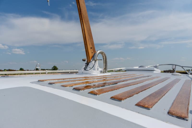 Een detailfoto van het dek van een boot met een houten mast en houten latten op het dek.