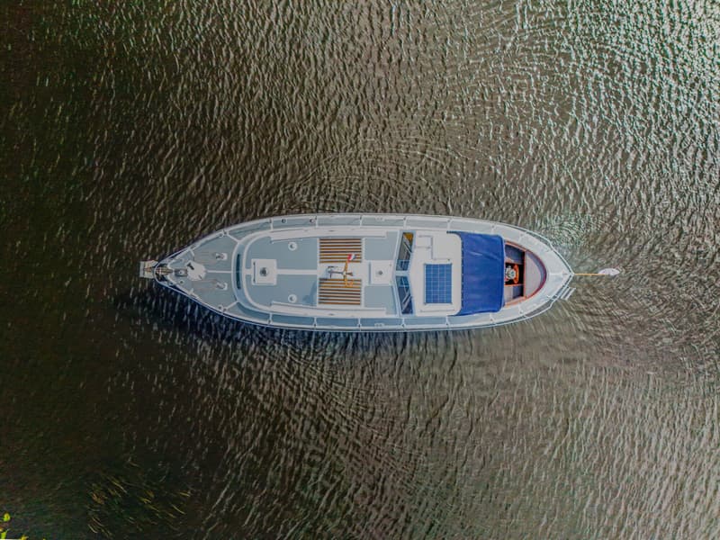 Een bovenaanzicht van een boot met een blauw dekzeil en een zonnepaneel, drijvend op rimpelend water.