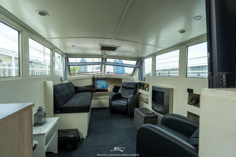 De foto toont een interieur van een boot met een zithoek, ramen, een bed en een open haard.
