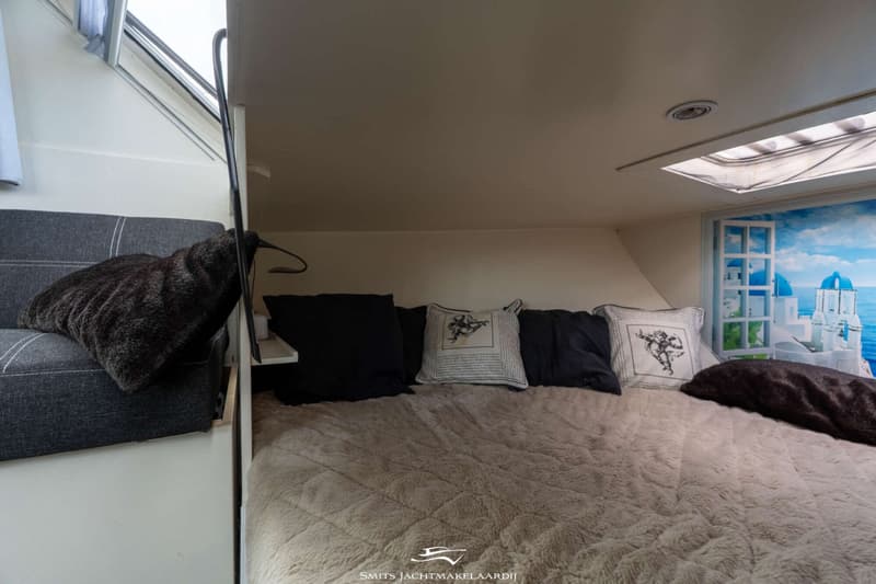 Een slaapkamer met een tweepersoonsbed, kussens en een raam met uitzicht op een Grieks landschap.