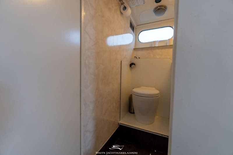 Een toiletruimte met een wit toilet, een toiletrolhouder en een raam.
