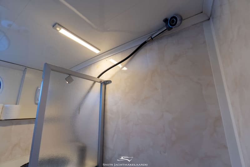 Een detailfoto van een douchecabine met een glazen deur, een douchekop aan het plafond en een lichtbalk.