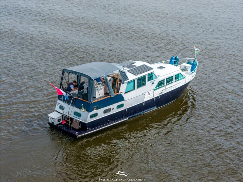 Een blauw-witte motorboot met de naam "Jottum" vaart op het water, met zonnepanelen op het dak.