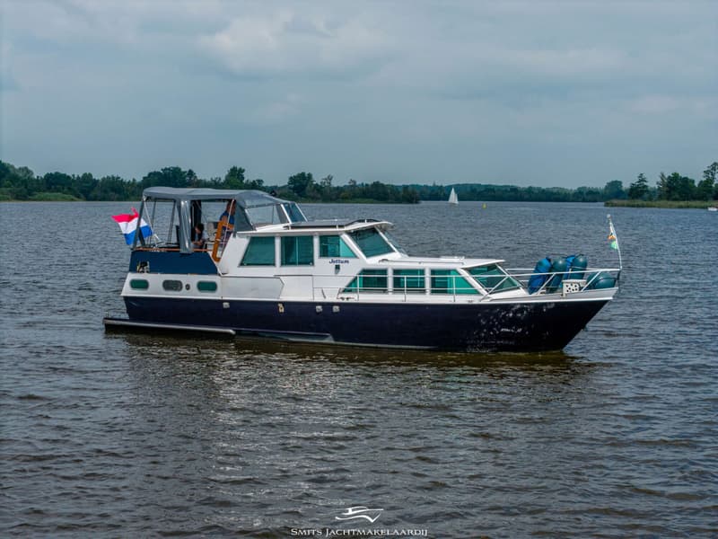 Een donkerblauwe en witte motorboot met de naam "Jottum" vaart op een meer onder een bewolkte hemel.