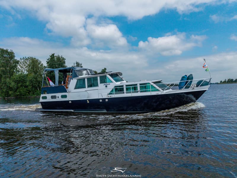 Een donkerblauwe en witte motorboot met de naam "Jottum" vaart over het water, met een vlag aan de boeg.