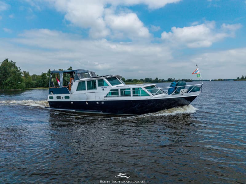 Een donkerblauwe en witte motorboot met de naam "Jottum" vaart over het water, met een vlag op de boeg.