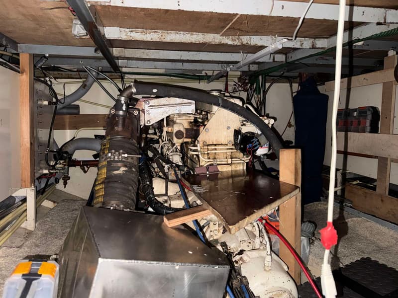 De foto toont een motorruimte met een grote motor, diverse slangen, kabels en leidingen, en een metalen tank op de voorgrond.