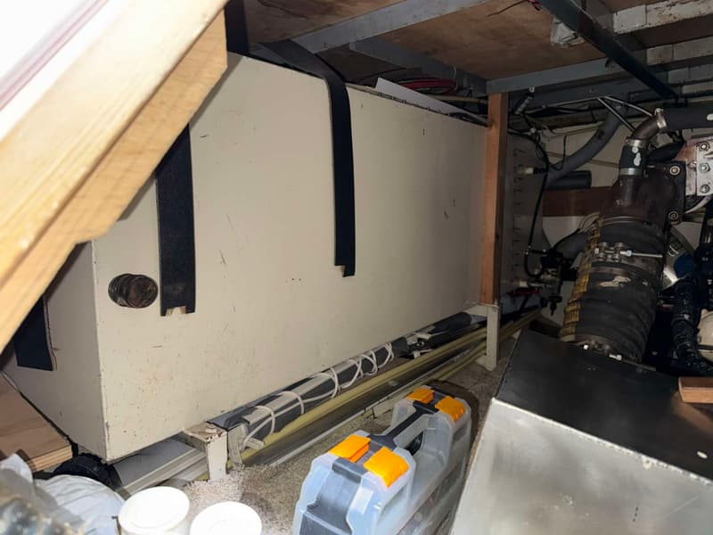 Een witte tank met zwarte banden is zichtbaar, met leidingen en een gereedschapskist op de vloer.