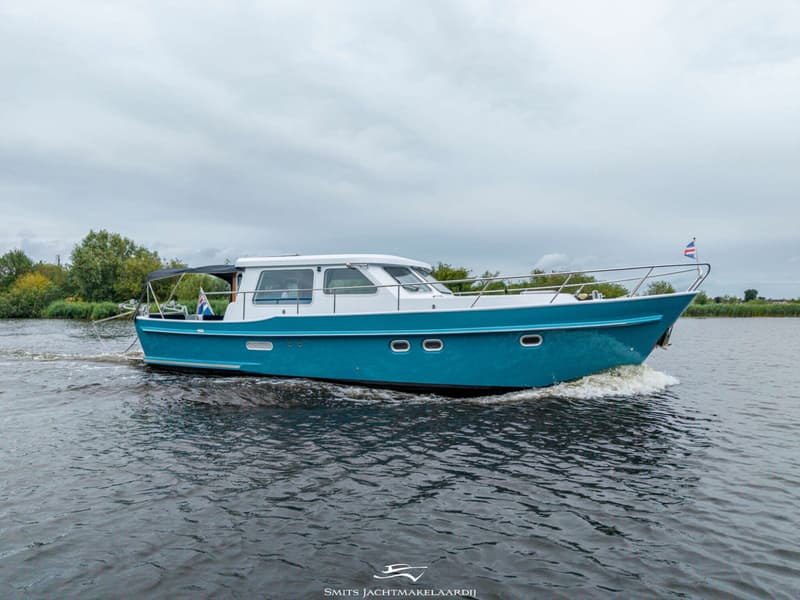 Een blauw-witte motorboot vaart op het water, met een Nederlandse vlag aan de boeg.