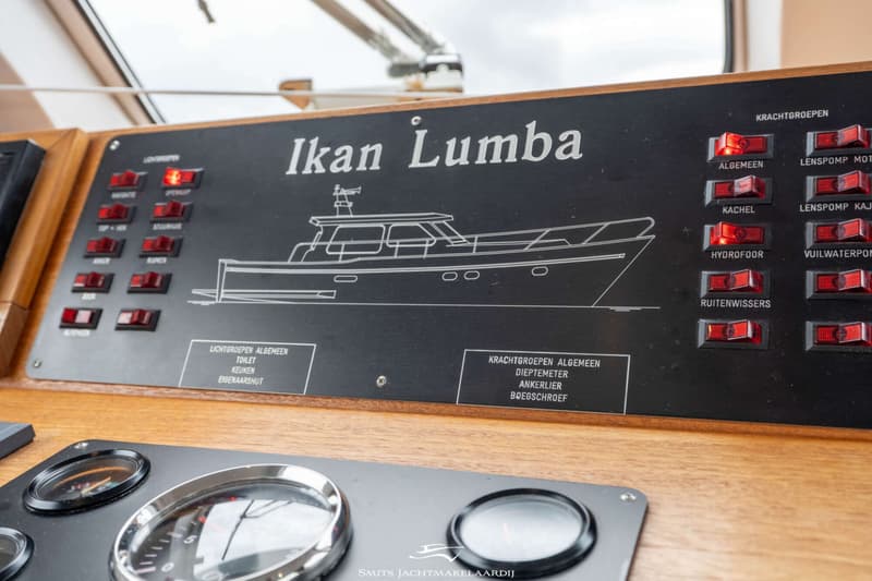 Een zwart bedieningspaneel met witte tekst "Ikan Lumba" en een schematische tekening van een boot, omringd door rode…