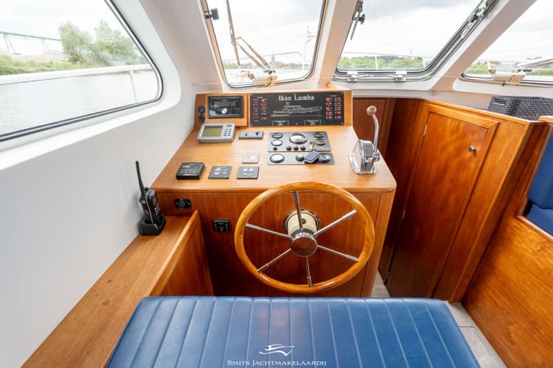 Een houten stuurwiel en een blauwe gestreepte bank in de kajuit van een boot. — Van Vossen Van Vossen Patrouille 10.50 OK