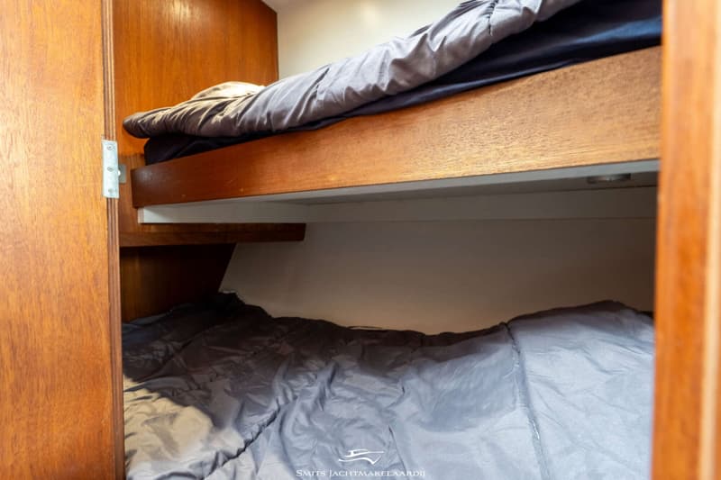 De foto toont een kajuit met twee stapelbedden, voorzien van grijs beddengoed, omringd door houten panelen.