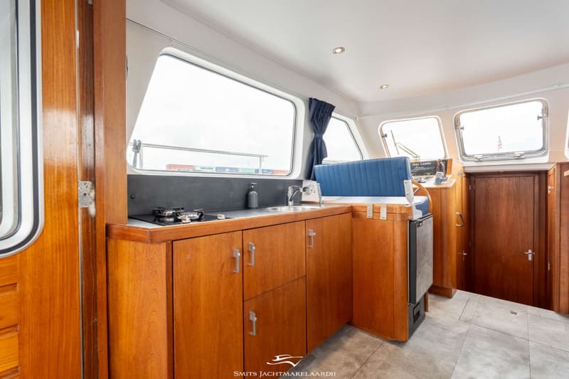 Een interieur van een boot met een houten keukenblok, een blauwe bank en een stuurstand.