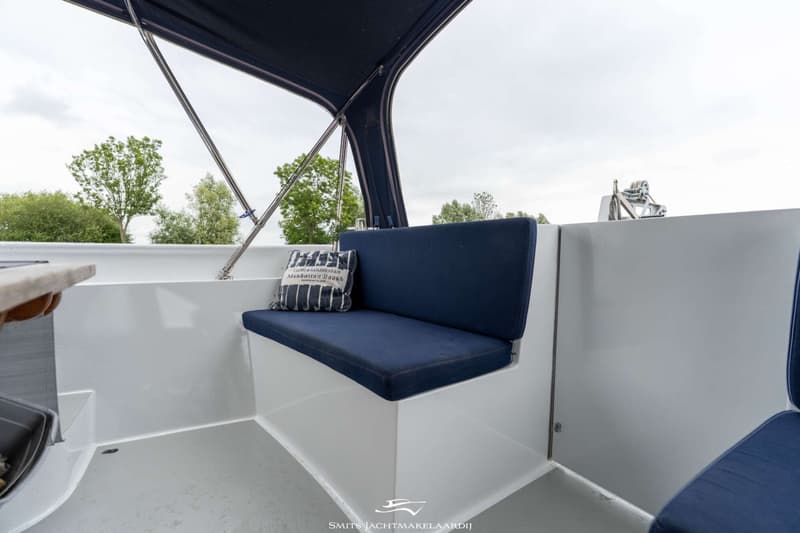 Een bootinterieur met blauwe kussens op witte banken, een donkerblauw afdak en een kussen met tekst.