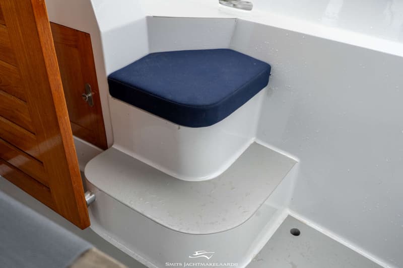 Een blauw kussen ligt op een wit bankje met twee treden ernaast, naast een houten deur.