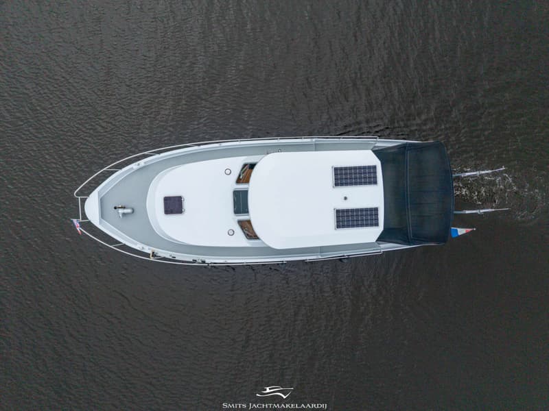 Een witte boot met een grijs dek en een zwarte kap, gezien van bovenaf op het water.