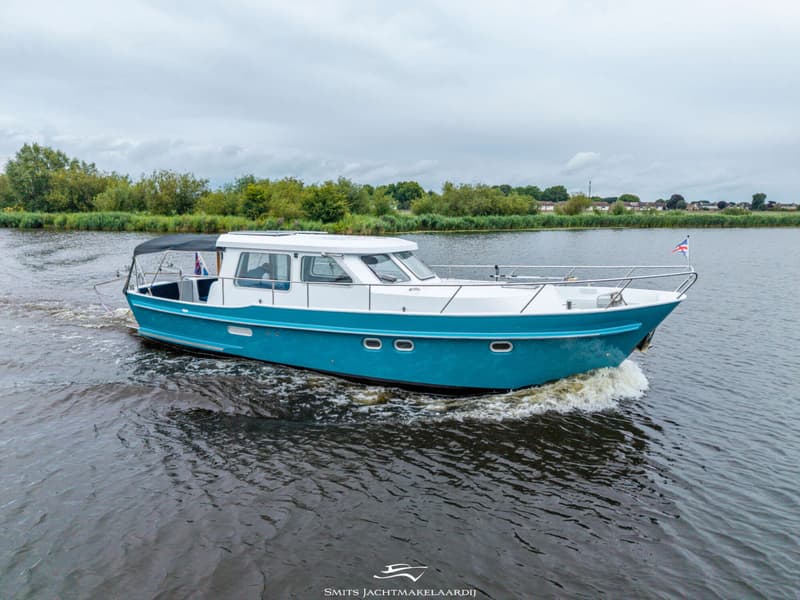Een blauw-witte motorboot vaart op een rivier met groene oevers onder een bewolkte hemel.