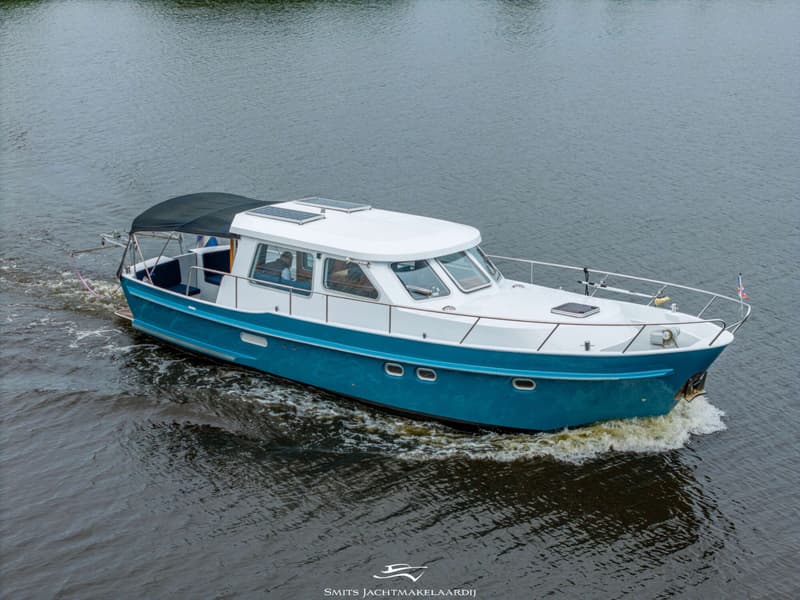 Een blauw-witte motorboot met een zwarte bimini vaart op het water, gezien vanaf een hogere positie.