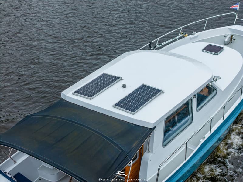 Een bovenaanzicht van een witte boot met blauwe accenten, twee zonnepanelen op het dak en een donkerblauwe bimini.