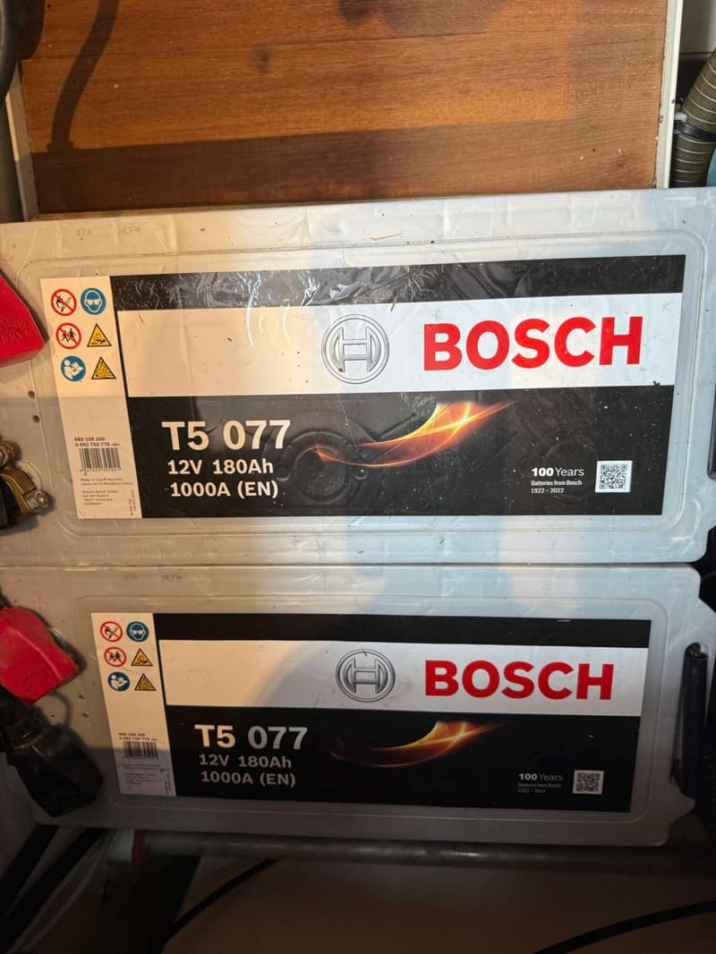 Twee Bosch T5 077 12V 180Ah 1000A (EN) accu's zijn zichtbaar, met waarschuwingssymbolen en productinformatie.