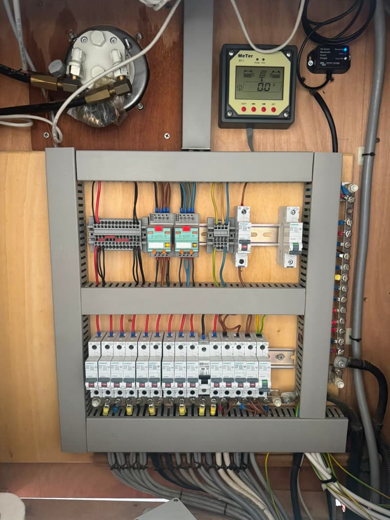 Een detailfoto van een elektrisch paneel met zekeringen, draden, een meter en een Bluetooth-dongle.