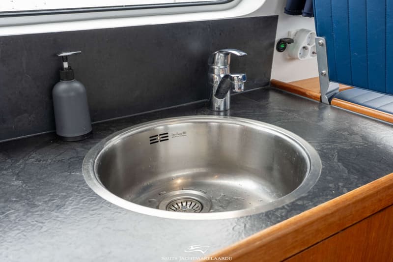 Een roestvrijstalen spoelbak met kraan en een zeepdispenser op een donker aanrechtblad.