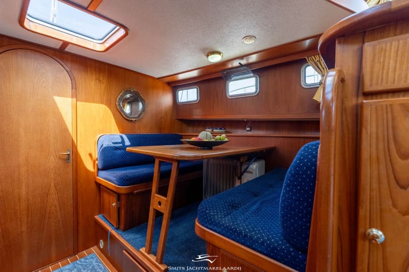 Een kajuit met houten wanden, een tafel, blauwe banken, ramen en een dakluik. — Babro yachting Babro Classic 13.40 AK