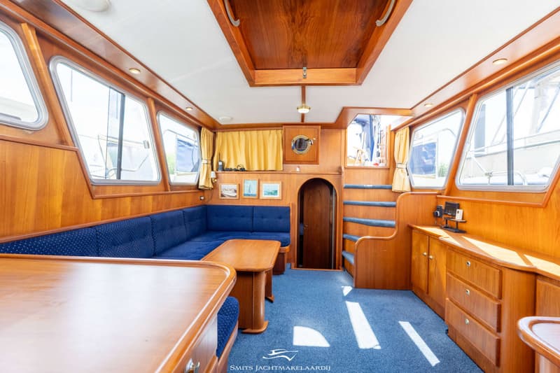 De foto toont het interieur van een boot met houten wanden, een blauwe bank, een houten tafel en een blauw tapijt.