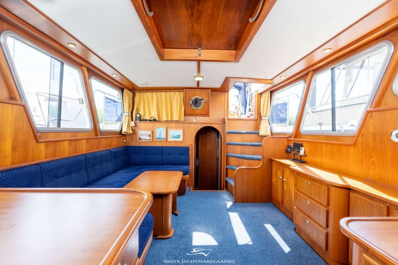 De foto toont het interieur van een boot met houten wanden, een blauw tapijt, een blauwe bank en een houten tafel.