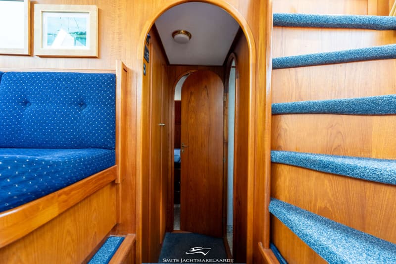 Een interieur van een boot met een blauwe bank, een houten trap met blauwe treden en een open houten deur.