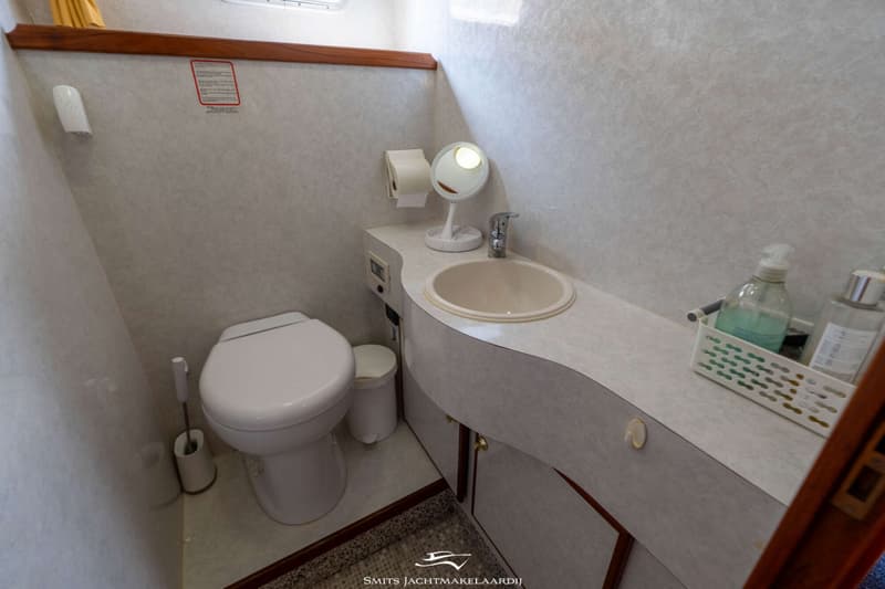 Een badkamer met een toilet, wastafel, spiegel, toiletrolhouder en een prullenbak.