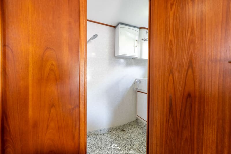 Een badkamer met een douchekop, een wastafel met kraan en een spiegelkast, gezien door een open houten deur.