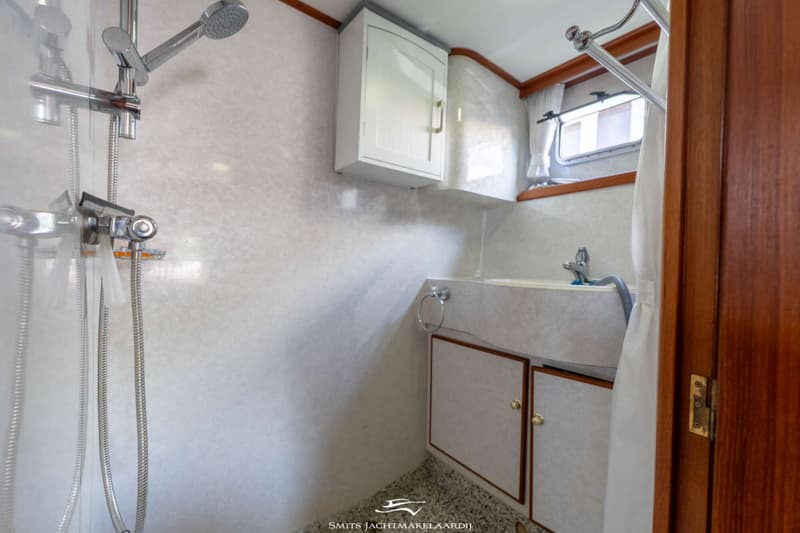Een badkamer met een douche, wastafel met kraan, spiegelkastje en een raam met gordijn.