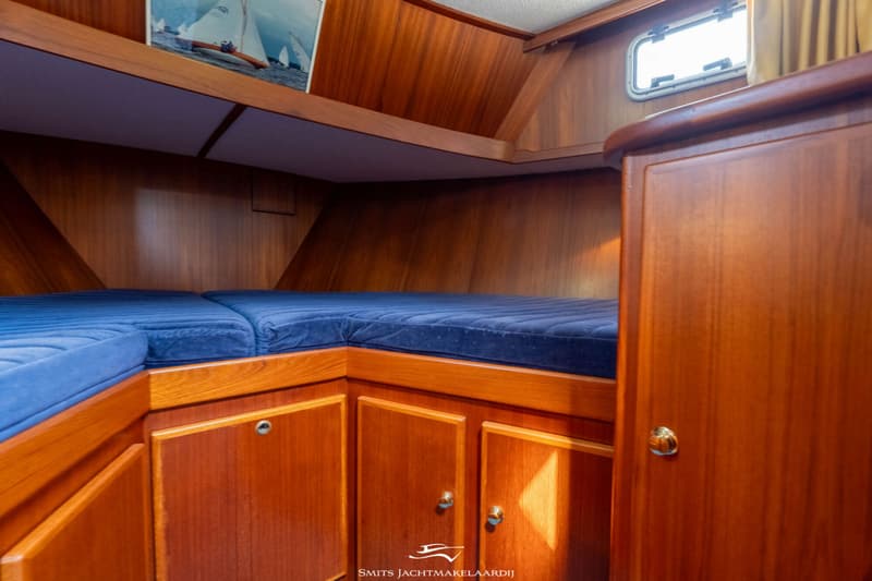 Een kajuit met twee blauwe matrassen, houten wanden, kasten en een raam met gordijn. — Babro yachting Babro Classic 13.40 AK