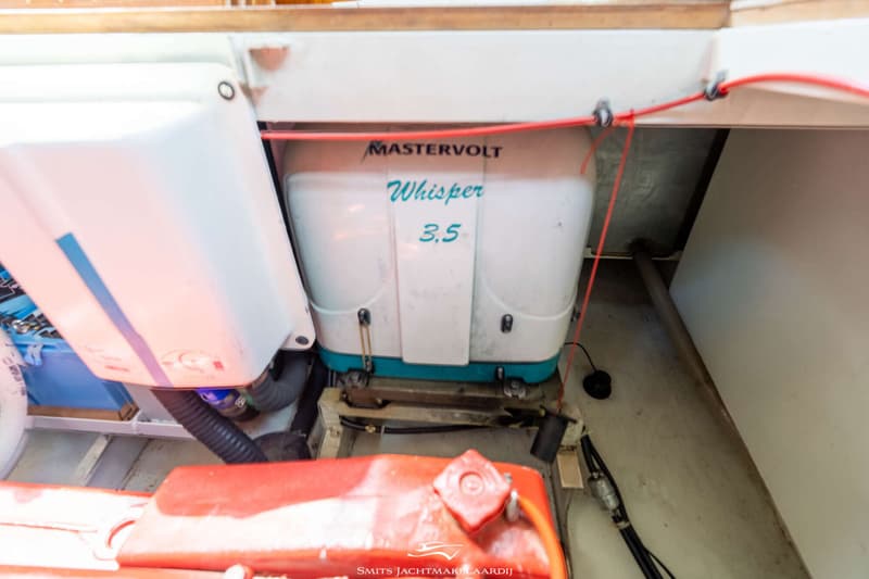 Een witte Mastervolt Whisper 3.5 generator staat op een houten frame, met een rode brandstoftank op de voorgrond.